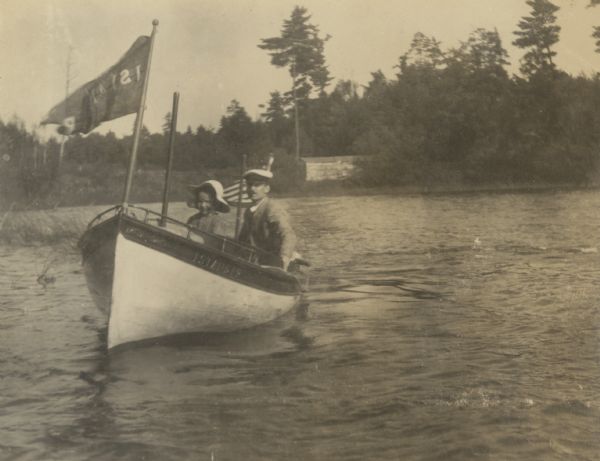 Donald Holt is steering the "Islander" motorboat with his father W.A. Holt at his side. The "Islander" flag is flying off the bow, and the American flag is flying off the stern. Caption reads: "Captain and Pilot."