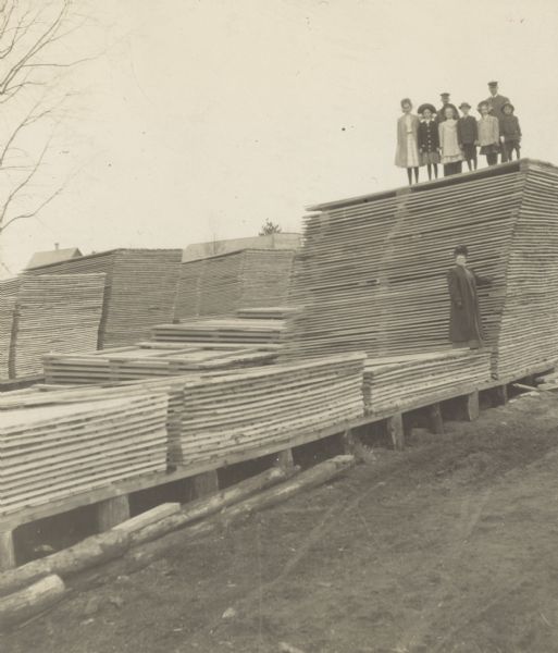 A group of adults and children is standing on the lumber piles. Caption reads: "Lumber piles."