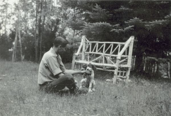 The Holt family dog, a Spaniel named Sketch, is chewing on something that Donald Holt is holding. An outdoor bench, made of birch wood, is in the background. Caption reads: "Don H and Sketch."
