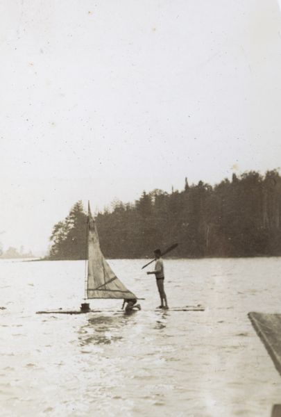 Two boys are sailing a homemade boat on Archibald Lake. Forested lands are in the background.