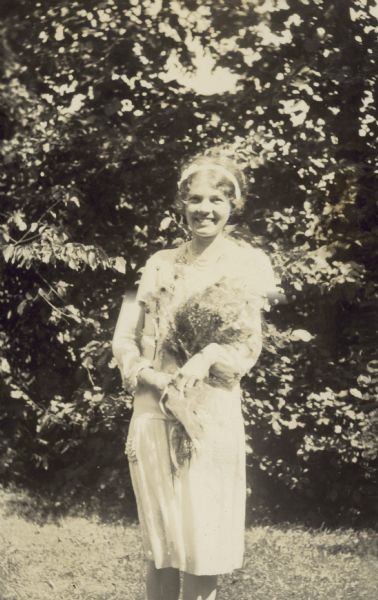 Elizabeth Dorsey, one of Eleanor Holt's bridesmaids, is standing outdoors holding a bouquet of flowers.
