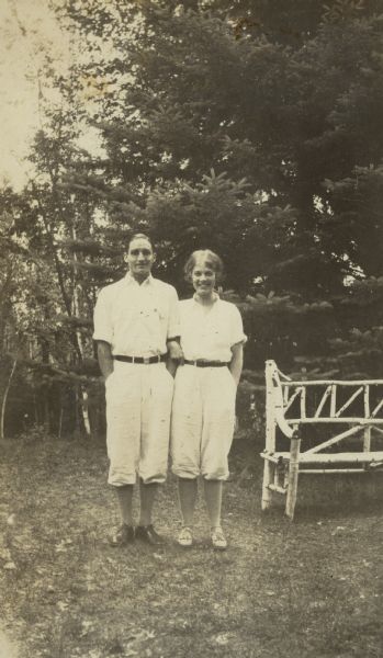 Donald Holt and Elizabeth Dorsey are standing side by side, arm in arm, wearing similar sportswear. An outdoor bench, made of birch, is on the right, and a tall pine tree is in the background. Caption reads: "Don and Elizabeth."

