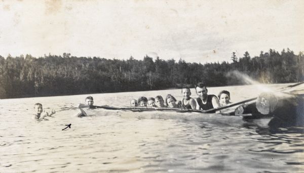 W.A. Holt, second from the right, and a group of mostly children are playing in Archibald Lake. On the far left, Alfred Holt is giving a thumbs up, with a cylindrical object floating in front of him. W.A. Holt is between Donald Holt (l) and Jeannette Holt (r). Caption reads: "Riding the 'Kentucky Mule.' A Jolly Bunch."