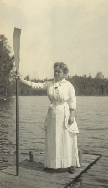 A woman, possibly Mrs. Buswell, is holding a boat oar with her right hand, resembling a monarch with a scepter, while standing on the pier. Archibald Lake is in the background. Caption reads: "The Dove of the Ark."
