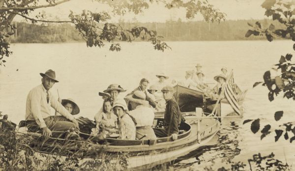 Looking at the camera, G.F. Loomis is sitting in the front of boat, on the far left. In total, there are 4 boats arriving at Picnic Island on Archibald Lake. Caption reads: "Landing at Picnic Island."