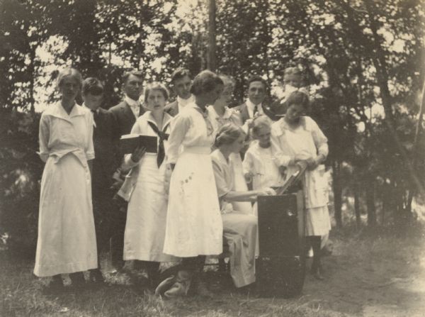 Jeannette Holt is sitting and playing the organ during a hymn sing on the Island. Family and friends are gathered around her. Names from left to right: Margaret Stroh, Alfred Holt, W.A. Holt, Juliet Rumsey Stroh, Oliver Buswell, Eleanor Holt, Harriet Stroh, Lillian Wheeler, Karl Buswell, Mr. James O. Buswell, and Juliet Stroh.