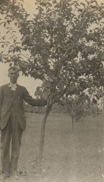 W.A. Holt is standing a field holding onto a fruit tree. 