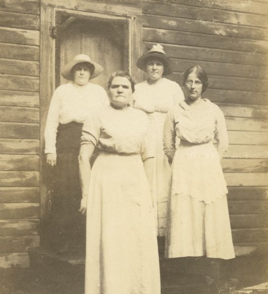 Group portrait of four household employees posing in front of the door of a cabin.