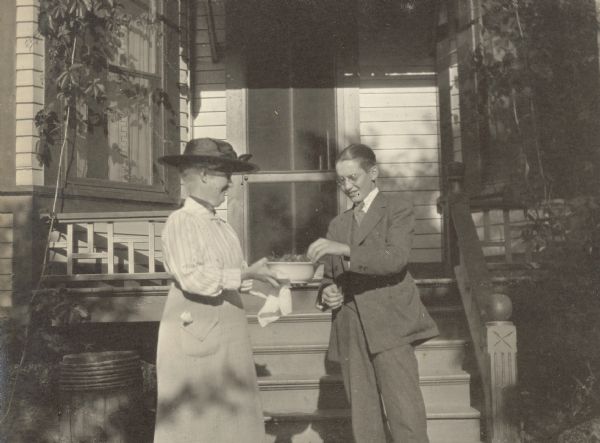 Donald Holt, who is 16 years old, is wearing his first long trousers, marking the transition from boyhood to manhood. He is taking a strawberry that Mrs. W.K. Smith is offering to him. Caption reads: "Strawberries and First Long Trousers. Mrs. W.K. Smith and DRH."