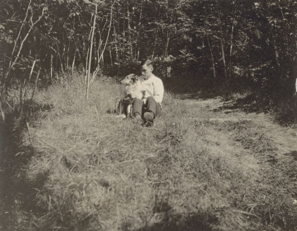 Gordon Wheeler is sitting on the ground in a clearing by a wooded area with his Collie named Queenie. Caption reads: "Gordon Wheeler and Queenie."