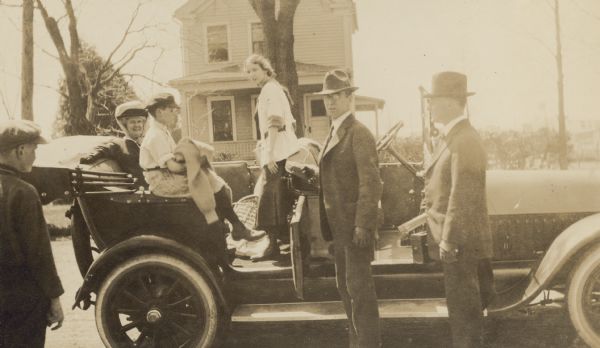 The group of people with sn automobile appears to be coming home after an outing, possibly to the Arbutus Mineral Spring in Oconto. W.A. Holt is opening the car door. Names from left to right: Unknown, Mrs. W.K. Smith, Donald Holt, Eleanor Holt, W.A. Holt, Rev. E.W. Wright. Caption reads: "After Arbutus."