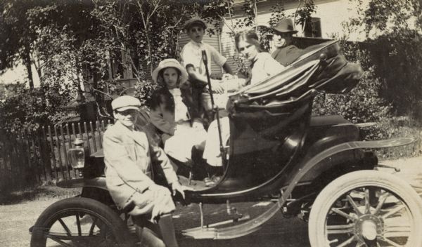 The entire Holt family, except photographer Lucy Rumsey Holt, is squeezing into the car. Lucy Rumsey Holt was the principal driver of this electric car. Names from left to right: Alfred Holt, Eleanor Holt, Donald Holt, Jeannette Holt, and W.A. Holt. The caption reads: "The Electric." 