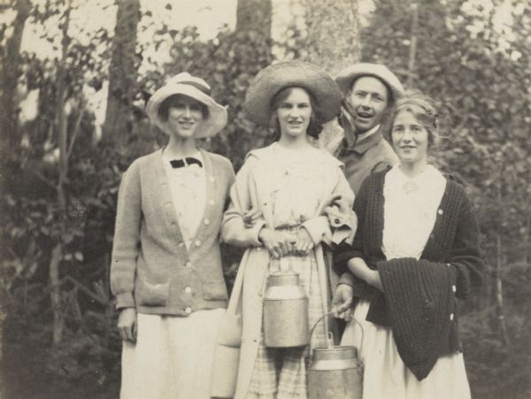 An informal group portrait of some of the Holt and Stroh cousins, along with Uncle Wallace Rumsey. Jeannette Holt and Wallace Rumsey are holding metal milk cans, which may contain a cold beverage such as lemonade. Caption reads: "Margaret Stroh, Jeannette Holt, Uncle Wallace, Harriet Stroh."