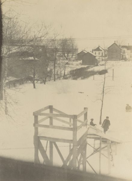 View of the backyard toboggan slide from the second floor of the Lucy and W.A. Holt home. Several people are in the snow at the bottom of the wooden slide.