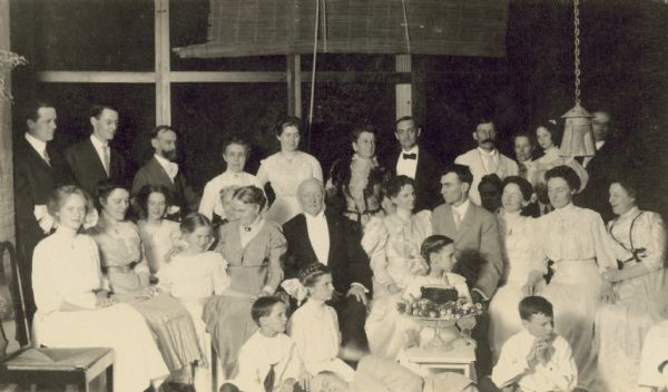 Lucy Rumsey Holt and W.A. Holt's 25th wedding anniversary. Three generations are present. A cake decorated with flowers is on display in front of Lucy and W.A. 

Caption from back to front, left to right, by row reads: 
"Neal Trowbridge, Wallace Rumsey, George Holt, Edna, Mrs. McClure, Dr. McClure, Arthur Wheeler, Sister Anna, Juliet Stroh - Grant. 

Margaret Stroh, Marion, Harriet Stroh, Cousin Sarah, Aunt Dena, Uncle Lilburn.

Elizabeth Stroh, Mother, Father, LRH, WAH, Minnie, Ellen, Harriet.

Donald, Jeannette, Eleanor, Alfred

Henry"