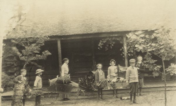 After gathering birch bark, a group of children and an adult are returning to Island Lodge. One boy is pushing a wheelbarrow. Caption reads: "Birch bark gang."