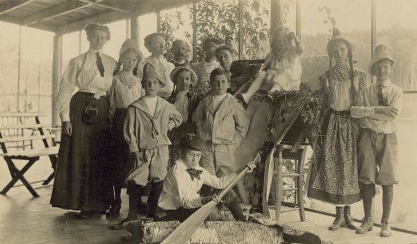 Group portrait of Holt and Wheeler children who are dressed in costumes to resemble young Germans. One boy, sitting on the floor in front, is pretending to paddle a birch bark canoe. There are several adults in the back row. Caption reads: "German dinner and Entertainment at 'The Ark.'"