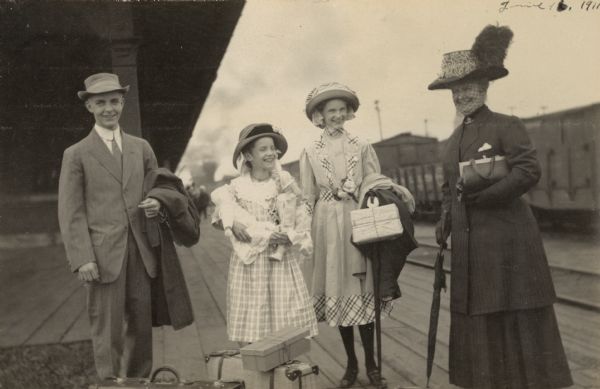 A group of travelers are standing on a platform, with the train station in the background. Names from left to right: Philip Smith, Eleanor Holt, Jeannette Holt, and Mrs. W.K. Smith. Caption reads: "Phillip, Eleanor, Jeannette, Mrs. W.K. Smith."