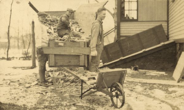 Title reads: "The Two Dons" for Donald Holt and Donald DeWitt. Donald Holt is standing on the left. He and another boy are carrying the box filled with wood scraps. The third boy is sitting on the wood pile in the background.
