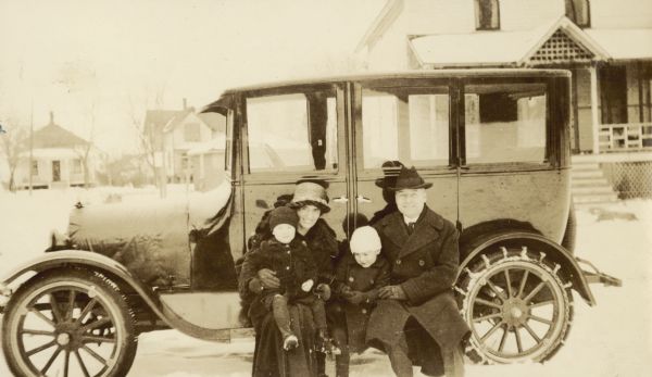 Rev. Ernest W. Wright and Rheua Nickey Wright are sitting on the running board of the car with sons William and Robert. The car has snow chains on the tires. Caption reads: "Rev. and W. Wright - William and Robert."