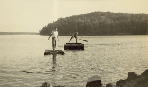 Two young men are playing around on the water on two rafts.