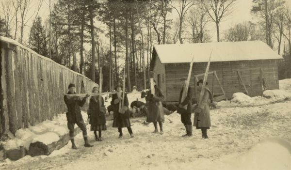 A group is visiting one of the Holt Lumber Camps on a winter day. Each person is holding a large icicle. Names from left to right: Unknown, Eleanor Holt, Unknown, Unknown, W.A. Holt, Jeannette Holt. Caption reads: "Camp 1."