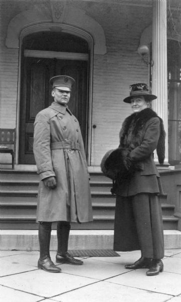 Alfred Holt, in uniform, and his aunt Ellen Holt are standing in front of the I.P and Mary Mathilda Rumsey family home, which was called "The Evergreens." She was active in the settlement house movement in Chicago. Caption reads: "Alfred and 'Aunt Nell.'"