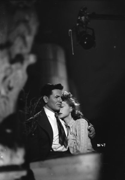 Lili Palmer is resting her head on John Garfield's shoulder in a scene from the 1947 film "Body and Soul." A piece of equipment, possibly a microphone, is hanging above them on the right.