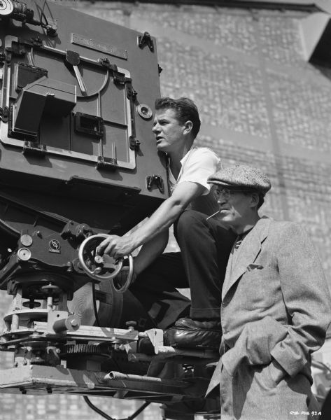 Camera operator Ted Moore and director John Huston, possibly at Isleworth studios in England, filming the 1951 film "The African Queen." Moore is operating a movie camera, and Huston is standing next to him