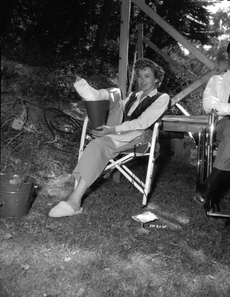 Director Ida Lupino sitting in a chair on the outdoor set of the 1949 film "Never Fear." She is resting her bandaged foot on a megaphone.