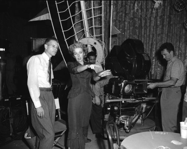 Director Ida Lupino on the set of the 1949 film "Never Fear." She is gesturing and talking to an unidentified man. A movie camera is on the right side of the image.