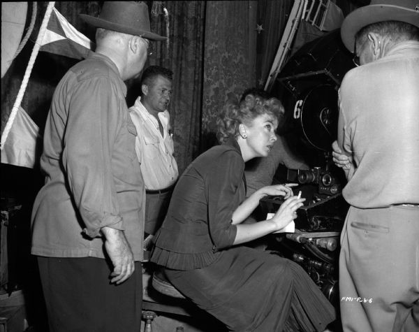 Director Ida Lupino is sitting at movie camera, surrounded by unidentified men, probably the film crew, on the set of the 1949 film "Never Fear."