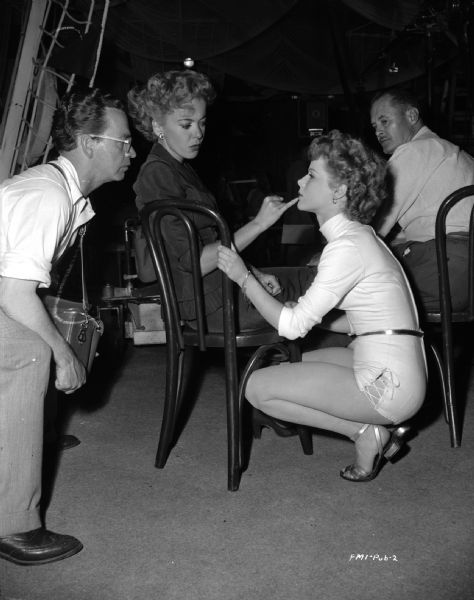 Director Ida Lupino is pointing to actor Sally Forest's lip on the set of her 1949 film "Never Fear." An unidentified man, possibly makeup artist James R. Barker, is crouching next to Lupino on the left.