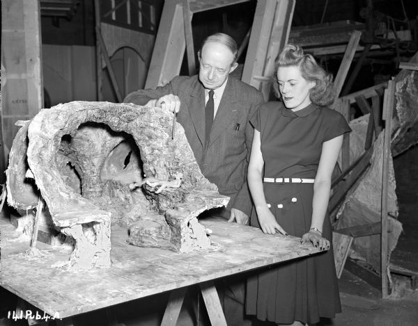 An unidentified man, possibly art director George Paterson, is showing producer Betty Box a scale model of the underwater cave set for the 1948 film "Miranda." The model also contains two figures.  