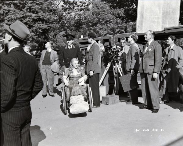 Actors Glynis Johns and David Tomlinson, and the film crew, waiting to film an outdoor scene from the 1948 film "Miranda." Men are around a movie camera in the center.