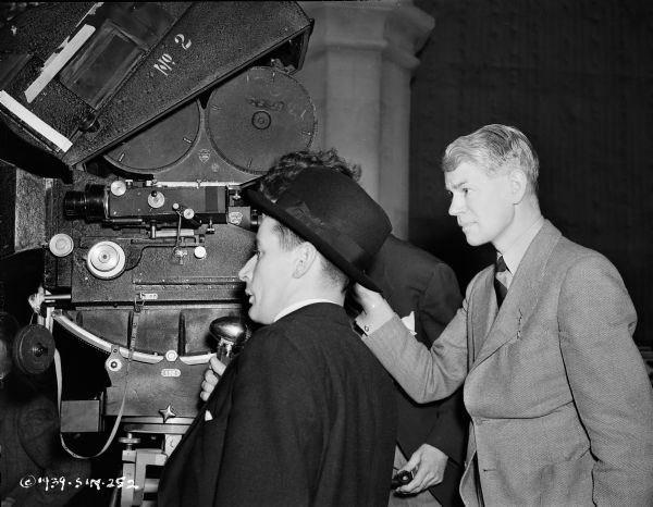 Director James Whale and the film crew during the making of the 1939 film "The Man in the Iron Mask." The men are standing around a movie camera, and one of them, (obscured) is holding what is probably a microphone.