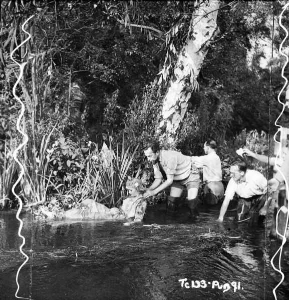Jeans Simmons with film crew, preparing to film a scene from the 1948 film "Hamlet." Ms. Simmons is in the process of lying down in a creek, to reenact the drowning of Ophelia.