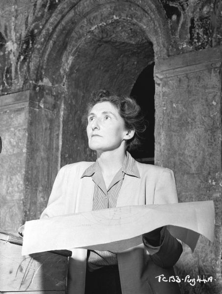 Art Director Carmen Dillon on the set of the 1949 film "Hamlet." She is holding blueprints while standing in front of an arch.
