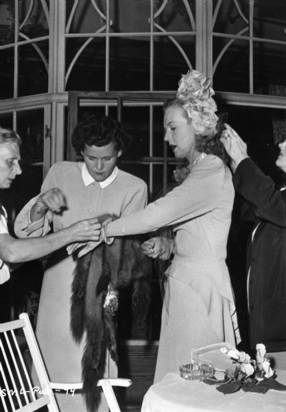 Unidentified actress having her gloves and veil adjusted by three other persons, on the set of "Sleep, My Love." One person is holding a fur stole.