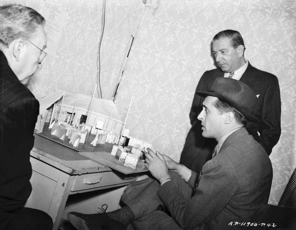 Director René Clair looking at a model of set from the 1944 film "It Happened Tomorrow." The model represents the interior of tent at a racetrack. 