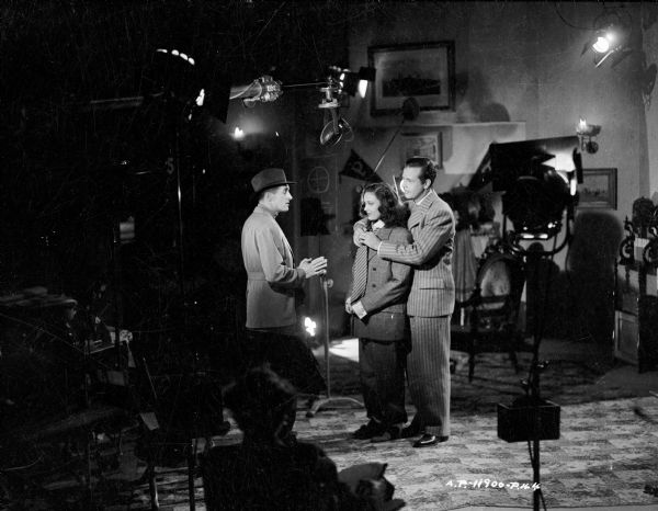 Director René Clair talking with actors Linda Darnell and Dick Powell on the set of the 1944 film "It Happened Tomorrow." A microphone is over their heads. 