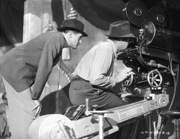 René Clair and an unidentified man during the making of the 1944 film "It Happened Tomorrow." Both men are behind a movie camera perched on a crane.