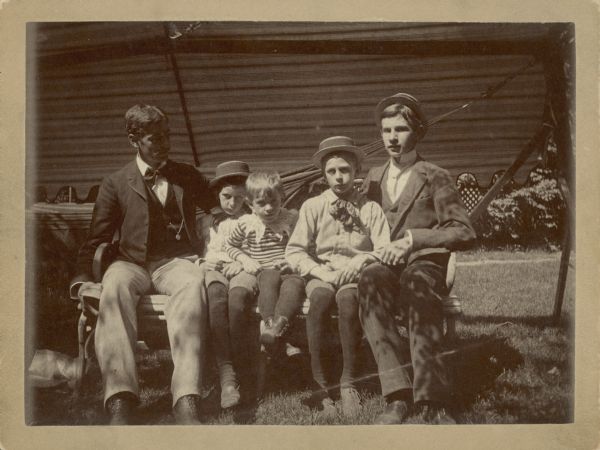 A group of five young men and boys, all sons of George and Henriette Brandhorst Brumder, sitting on a bentwood settee. A hammock and awning form the background. Identified on the reverse of the photograph, they are, from left, William Charles Brumder (1868-1929), Herman Otto Brumder (1880-1950), Herbert Paul Brumder (1885-1967), George Frederick Brumder (1878-1961) and Alfred Julius Brumder (1874-1897). Herman, George and Alfred are wearing hats. 
