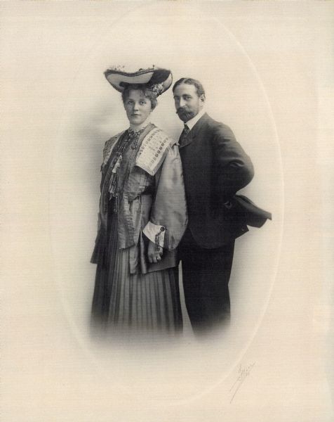 A copy of a standing, three-quarters length studio wedding portrait of Thekla Uihlein and William Charles Brumder. She is wearing a fancy dress and hat with large brim. He is wearing a suit and tie, and is holding his hat behind his back. Thekla was the daughter of August Uihlein, an owner, the secretary and chairman of the board of Schlitz Brewing Co.  William was the son of publisher George Brumder.  