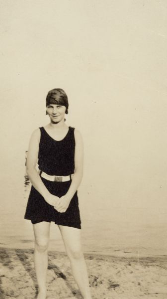 Marion Briggs is standing and posing wearing a swimming suit and bathing cap for a full-length photograph. On the reverse of the photograph is written: "Here's your picture taken at Bradford Beach. Will write later, Richard."