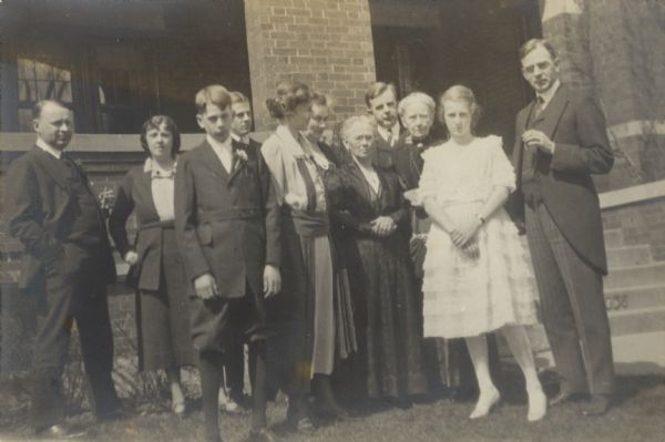 Edward John Brumder, third from left with boutonniere, and his sister, Henrietta Thekla "Pussy" Brumder, wearing a short white dress, posing with other family members on the day of their confirmation. Others in the group include, from left, their uncle John Wollaeger, aunt Florence Wollaeger; brother George Gustav Brumder; mother Thekla Wollaeger Brumder, aunt Lydia Wollaeger, grandmother Henrietta Thomas Wollaeger, uncle Herman Brumder, grandmother Henriette Brumder, and father George Frederick Brumder. The group is posing in front of the George F. Brumder residence on Grand (now Wisconsin) Avenue.