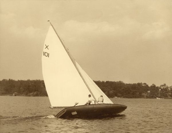 Three men, one hiking out, sailing the <i>Adventure</i> on Pine Lake. A note on the reverse of the photograph identifies Herby Brumder as skipper.  