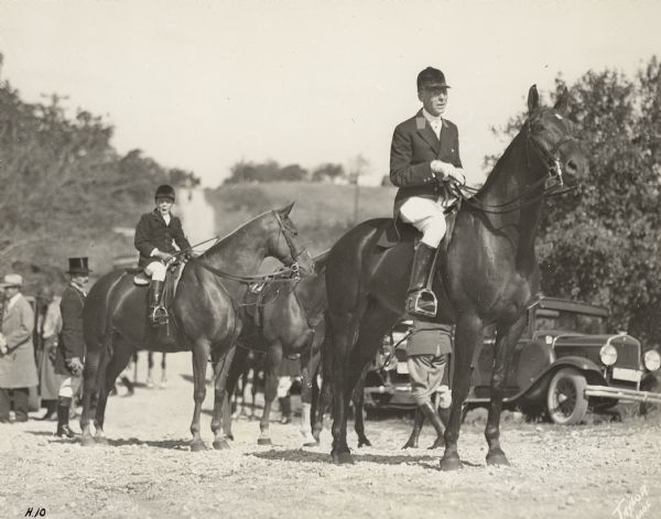 Member of the Milwaukee Hunt Club Frederick Pabst, Jr. (1869-1958), son of Captain Frederick Pabst, posing on horseback wearing traditional fox hunting attire. There is a similarly dressed young boy on horseback at left. There is another horse, two automobiles, and bystanders in the background. A notation on the reverse of the photograph reads: "Washington County Hunt, Fred Pabst."