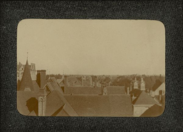 An elevated view, possibly in the area of 18th Street and Grand (now Wisconsin) Avenue, over the roofs of large homes. There is a large structure at left which may be a school or commercial building, and two church spires are on the right.