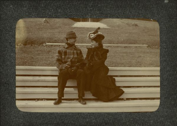 In a photograph labeled "Geo and Teck" George F. Brumder (1878-1961) is sitting and smiling with his wife Thekla Wollaeger Brumder (1879-1950) on the steps leading to Pine Lake. Behind them is the stone walkway to the porch of his parents' (George and Henriette Brumder's) summer home, Villa Henriette. They are wearing coats, gloves, and hats; Thekla has a fur stole.